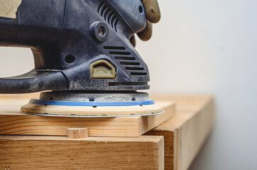 Joiner's tools. Sanding a wooden board with a hand-held electric sander