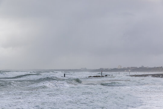 A dramatic view of a very choppy sea with huge crashing waves on groynes (breakwater) during a major storm under a grey sky
