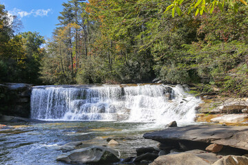 Obraz premium Early hints of autumn at the French Broad Shoals Waterfall in North Carolina.