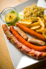plate with various types of frankfurters, potatoes, sauce and sauerkraut on wooden table. 