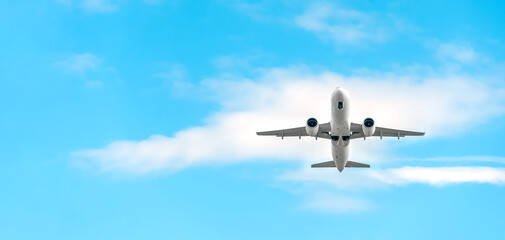 Low-flying white passenger plane with landing gear on a background of blue sky with clouds with copy space, bottom view. Plane took off and hides the landing gear in flight. Banner