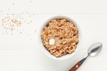 Wheat porridge with butter in a ceramic bowl on white wooden table. Healthy breakfast. Top view