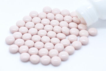 Pink pills scattered from a white jar on a white background