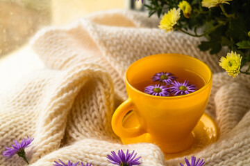 Yellow cup with herbal tea on a white knitted blanket on a rainy autumn day.