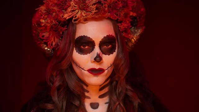 Beautiful image for a woman on All Saints' Day with makeup in the style of catrina calavera in the form of a decorated skull with a sewn mouth, horns and flowers close-up