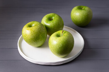 green apples on a flat  white handmade  plate on a gray wooden table