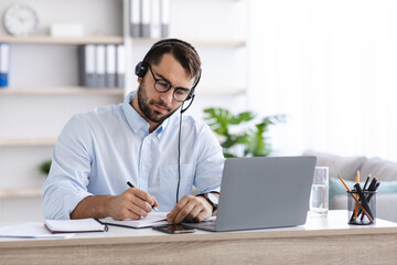 Busy middle aged european man with beard in glasses, headphones working at laptop