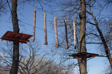 Children's attraction in forest. Wooden suspension bridge between trees, attached sticks on tree for signal. 