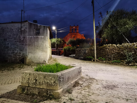 Antigo bebedouro para animais numa rua aldeia da aldeia de Selores com a Igreja paroquial ao fundo