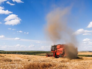Combine harvester removes wheat from the field and dust flies from under it.