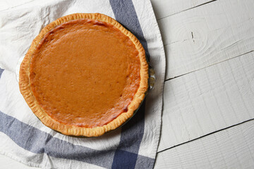 Fresh baked homemade pumpkin pie on a white wood table and tea towel. High angle shot with copy space.