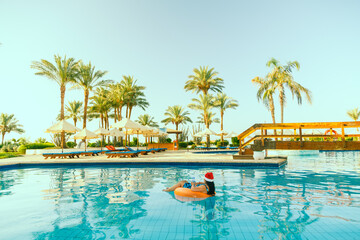 Young brunette woman in santa claus hat in a swimming circle in the pool during christmas holidays.