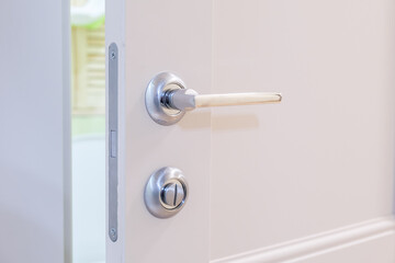 Slightly open white door to the bathroom with a metal magnetic lock. Chrome-plated handle on the interior door. Silent magnetic lock on the interior door.