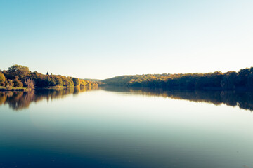 A row of colorful trees reflecting in the water at the Malomvölgyi-tó in fall, Pécs, Hungary