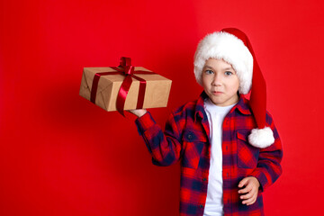 Happy holiday and Merry Christmas. Portrait of a boy in a cap with gifts in his hands on a red background. A place for text.