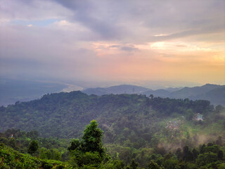 dramatic sunset orange sky over mountain range and green forest at evening from hill top