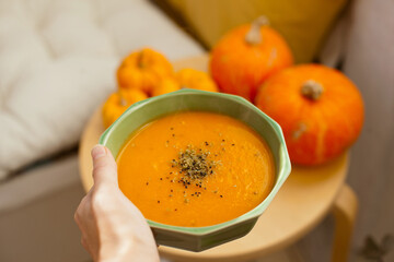 hand holding a bowl with pumpkin soup with pumpkins around it