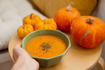 hand holding a bowl with pumpkin soup with pumpkins around it