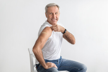 Vaccinated Senior Man Showing Arm Sitting Over Gray Studio Background