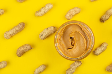 Bowl of peanut butter and scattered peanuts on yellow background