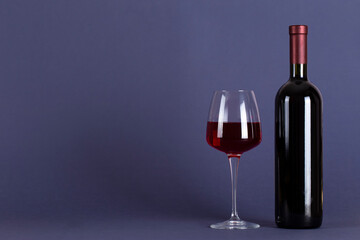 Closed bottle of red wine and a glass on a lilac background. With space for text.
