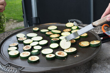 Preparing sliced zucchini on a grill. Hand moving the slices with tongs
