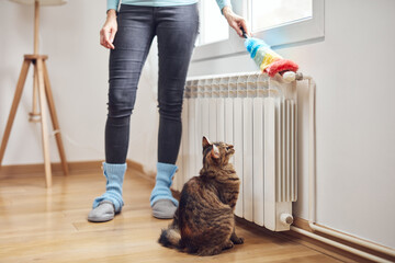 Woman with a dust stick cleaning central heating gas radiator at home.