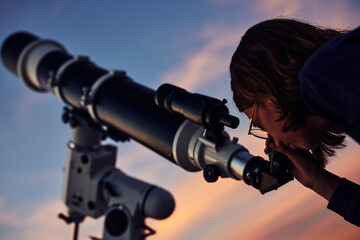 Girl with astronomical telescope stargazing under twilight sky.