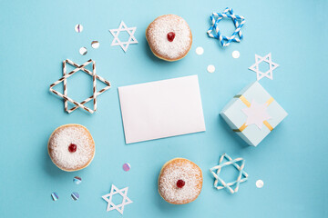 Jewish holiday Hanukkah concept - Hanukkah sweet doughnuts sufganiyot with powdered sugar and jelly fruit jam, gift box and empty white card on blue paper background.