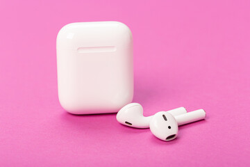 Modern wireless bluetooth headphones with charging case on pink background. The concept of modern technology.