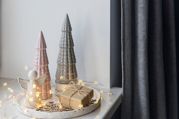 Earthenware gray and pink Christmas trees, garland, candles on a white round tray decorate the apartment for Christmas. Copy space