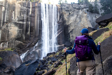 Middle-aged women hiking solo in the mountains near a waterfall and stops to enjoy the beauty.