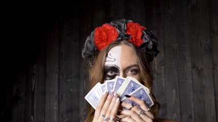 Lady model with skull makeup in red and black wreath choker and in lacy gloves shows gaming cards...