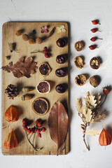 autumn still life composition with leaves, nuts, berries, cones and dry oranges on wooden board above white table
