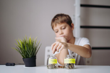 little caucasian boy putting coin into glass bottle at the table. Kid saving money for education