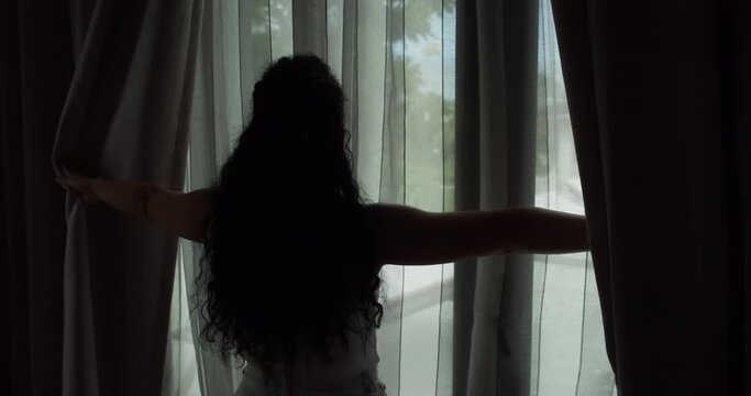 Young woman opening curtains in a bedroom. Closeup. Femele hands open window curtain in morning.Hands pulling a window curtain for warm morning light. Slow motion.