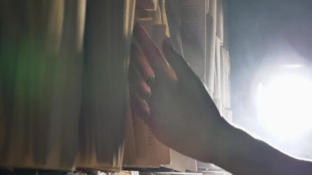 Young woman walks along storage wall with books attached and runs hand over old torn pages slowly at back light extreme closeup