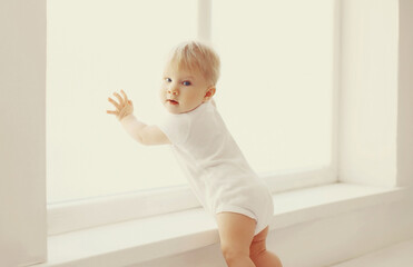 Fototapeta premium little baby touching window in white room at home