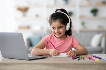 Naklejka premium Distance Education. Arab Female Child Wearing Headphones Study With Laptop At Home