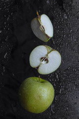 whole green apple, cut in half and  quarters on  black background with water drops with noise, grain and film effect, blurred, out of focus, flat lay, dark mood concept, vitamins and label add