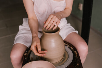 young girl in a white shirt makes a pitcher of clay on a potter's wheel. Pottery workshop of a creative woman. Concept - hobby clay modeling