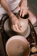 young girl in a white shirt makes a pitcher of clay on a potter's wheel. Pottery workshop of a creative woman. Concept - hobby clay modeling