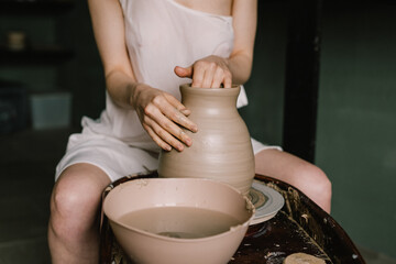 young girl in a white shirt makes a pitcher of clay on a potter's wheel. Pottery workshop of a creative woman. Concept - hobby clay modeling