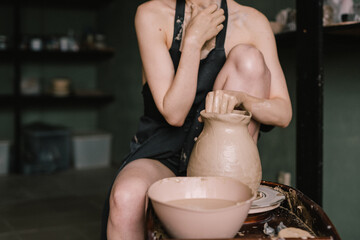 young girl in a black apron on her naked body sculpts a jug of clay on a potter's wheel. Pottery workshop of a beautiful woman. Concept - hobby pottery production