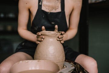 young girl in a black apron on her naked body sculpts a jug of clay on a potter's wheel. Pottery workshop of a beautiful woman. Concept - hobby pottery production