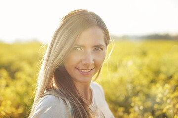 Portrait of young woman with long hair, yellow flower field and sun backlight behind her