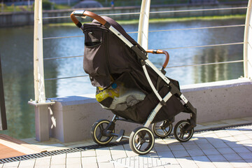 Black baby carriage, stroller on embankment near metal fence by water. Parenthood, motherhood,...