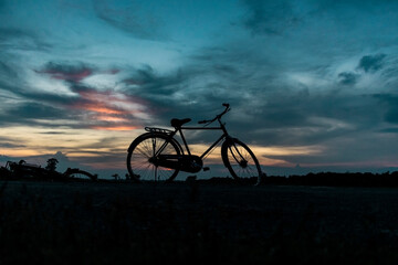 Naklejka na ściany i meble Bi-Cycle silhouette in front of sunset cloudy landscape
