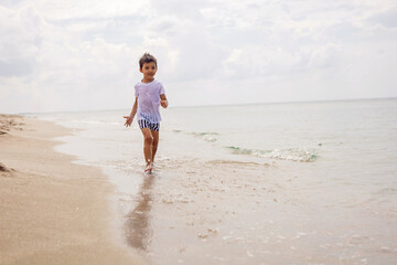 boy child in striped shorts and a white T-shirt walks on sandy beach and in sunglasses