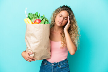 Girl with curly hair holding a grocery shopping bag isolated on green background with headache